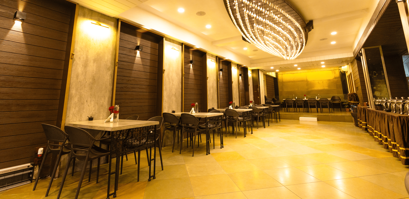 An indoor dining area with dining tables, chairs, and ceiling lights at Hotel Seagull Digha.