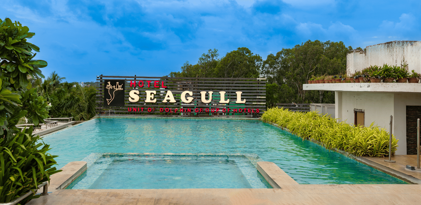 A swimming pool in front of the building with the ‘Seagull’ signage and trees in the background at Hotel Seagull, Digha.