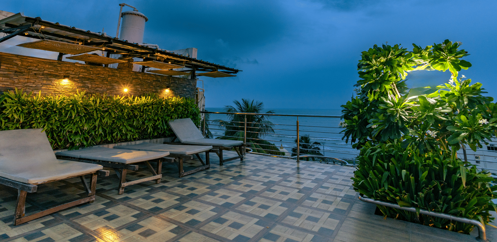 An outdoor seating area with tables, sun loungers, plants and a cloudy sky at Hotel Seagull Digha.