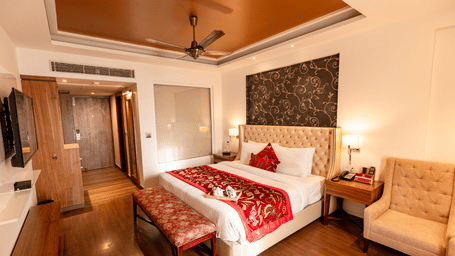 A bedroom with a king size bed, side tables, lamps, wall-mounted TV, armchair, and wardrobe arranged indoors at Indraprastha Resort & Spa, McLeod Ganj.