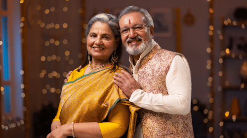 A middle aged couple posing in front of the camera for the renewal of vows. The walls at the background is lit with fairy lights and flowers.