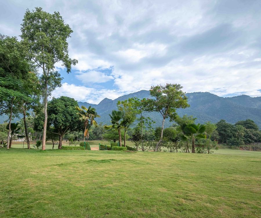 Large open lawn with a pathway leading into the distance, surrounded by trees and mountains in the background - Black Thunder, Coimbatore
