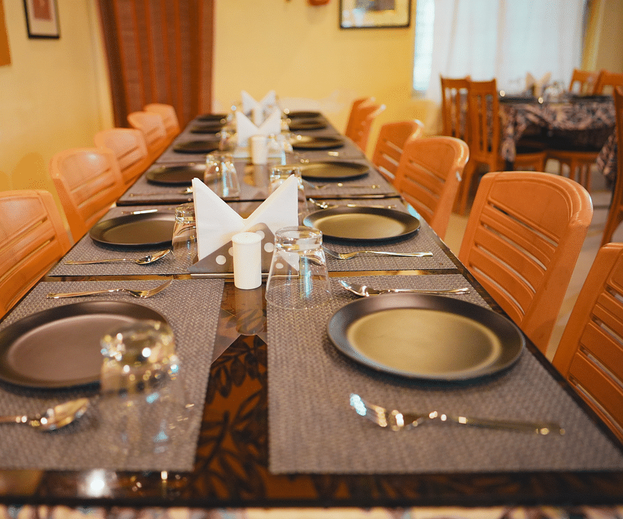 A cozy dining space featuring a rectangular table set with cutleries and surrounded by chairs on both sides, ready for a meal