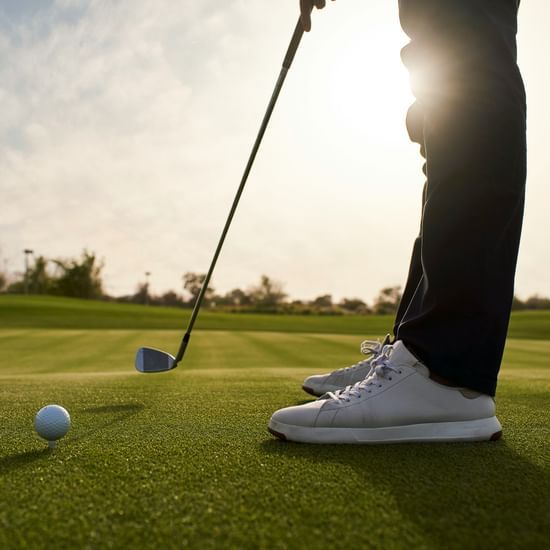 Golfer lining up a shot on a green course with the sun shining in the background.