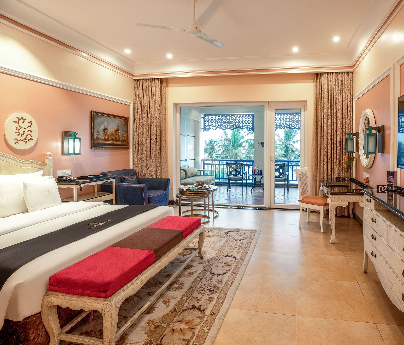 Spacious bedroom with seating area, a workstation, a ceiling fan, a wall-mounted TV, and large glass windows at MAYFAIR Palm Beach Resort, Gopalpur-On-Sea