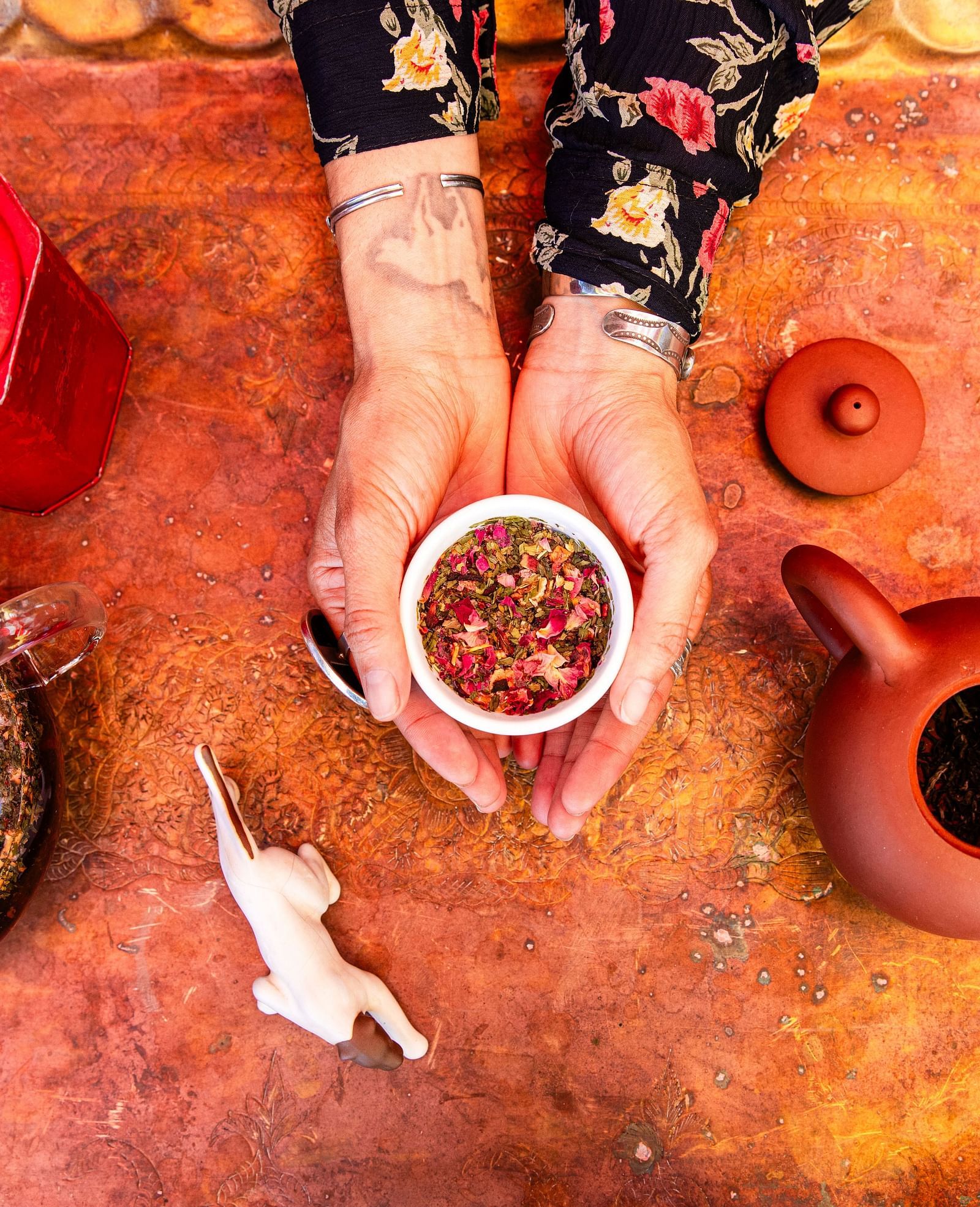 Overhead view of a vibrant tea table with clay cups, a teapot, and colorful fabric.