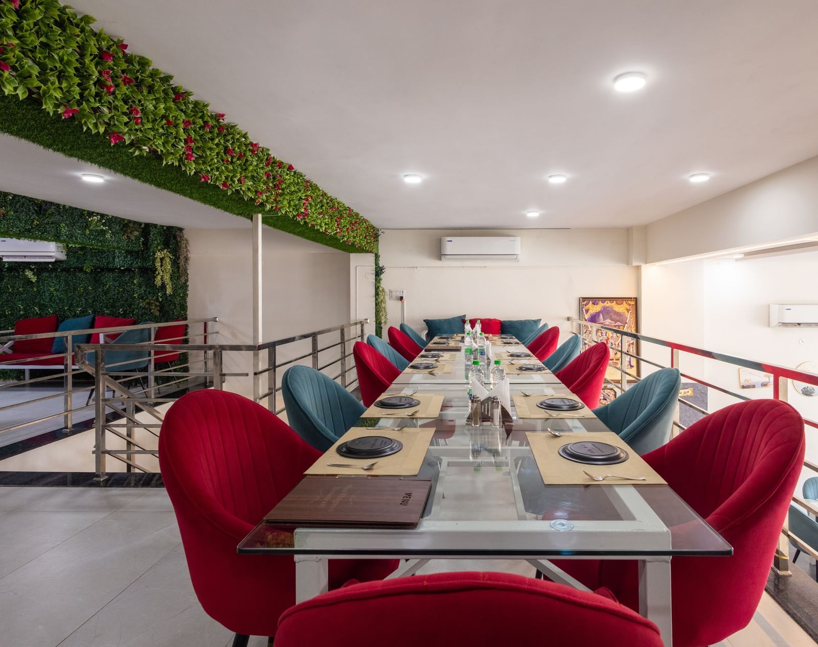 Long dining table setup with red & blue chairs and green decor on the wall at Pravasa Stay Dewas Naka, Indore.
