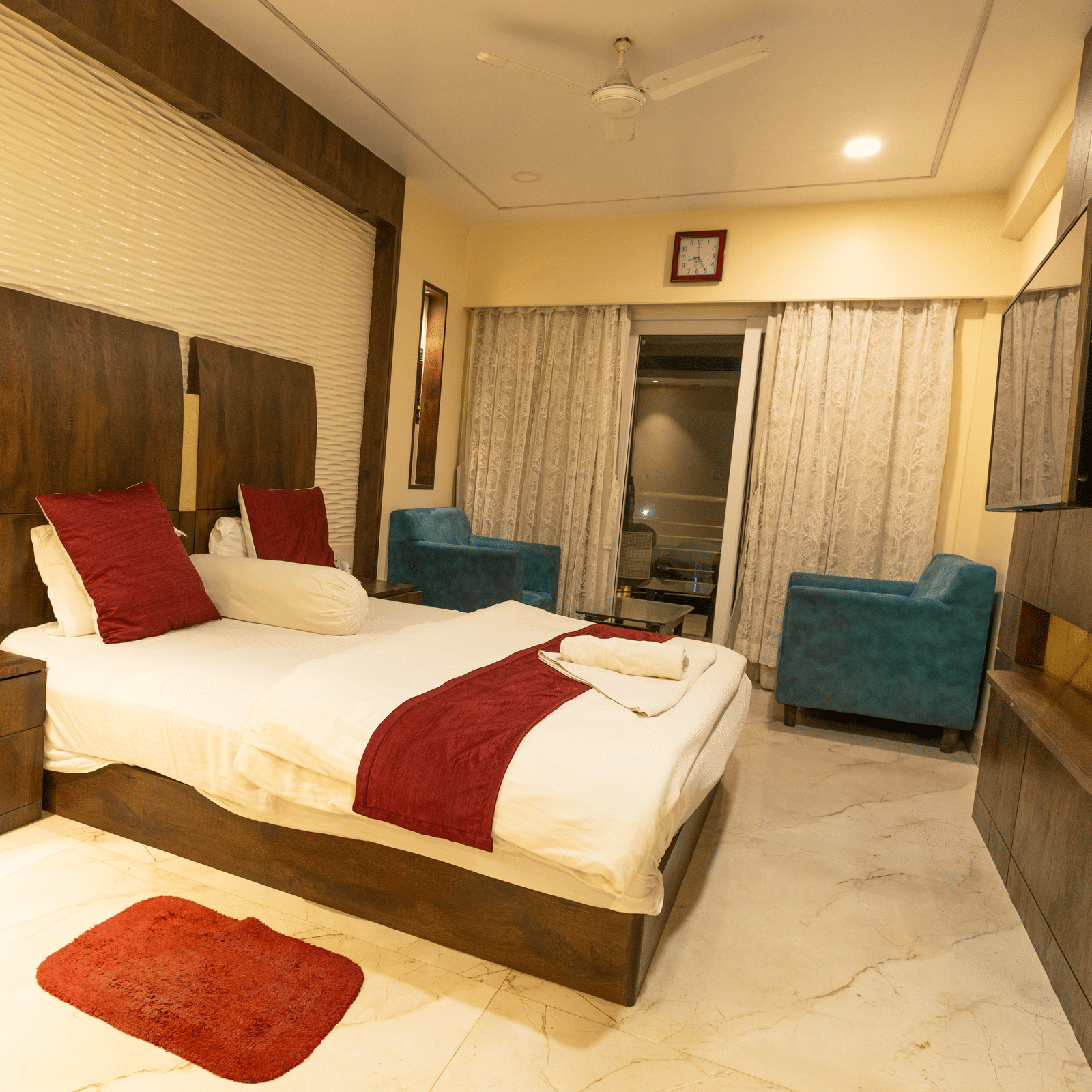 A bedroom with a king size bed, red cushions, a rug, 2 armchairs and a side table at Hotel Seagull Digha.