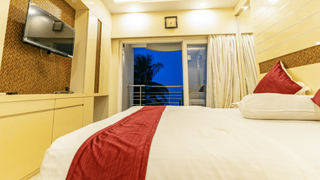 A bedroom with a king size bed with bedding, a television, and a window leading to a balcony at Hotel Seagull Digha.