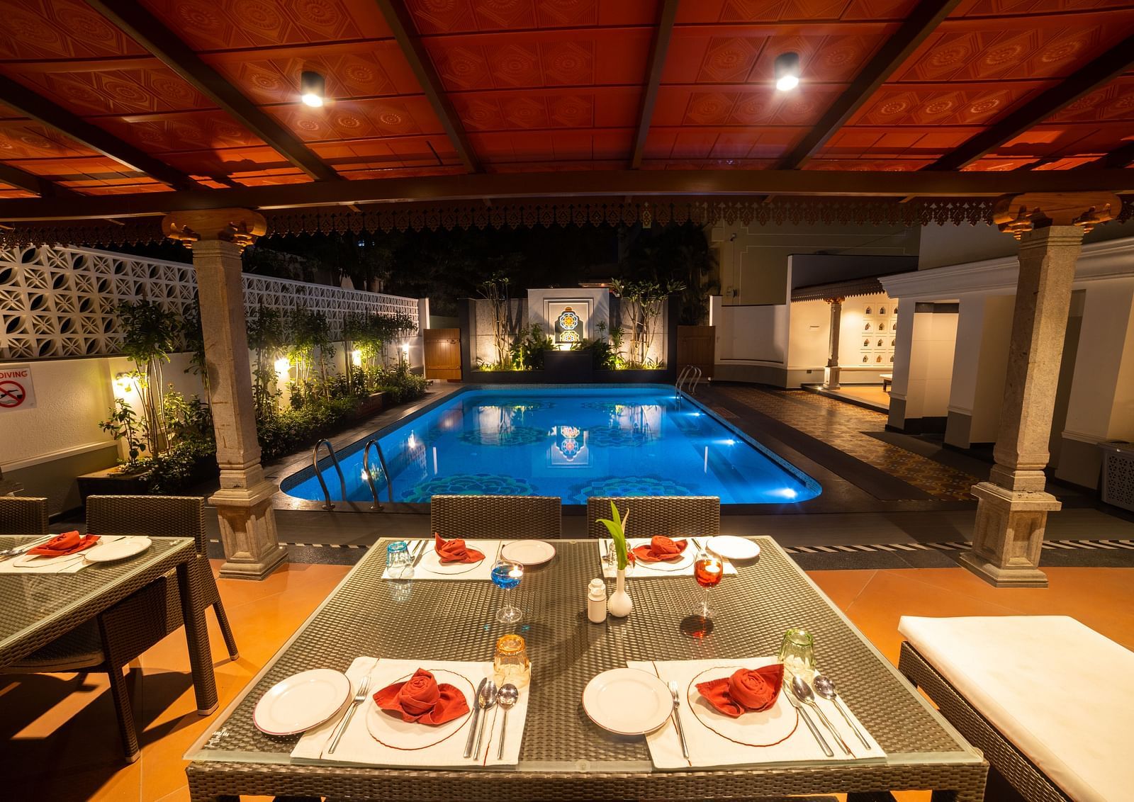 Poolside dining with a warm evening ambiance under a red canopy. Regency Madurai by GRT Hotels