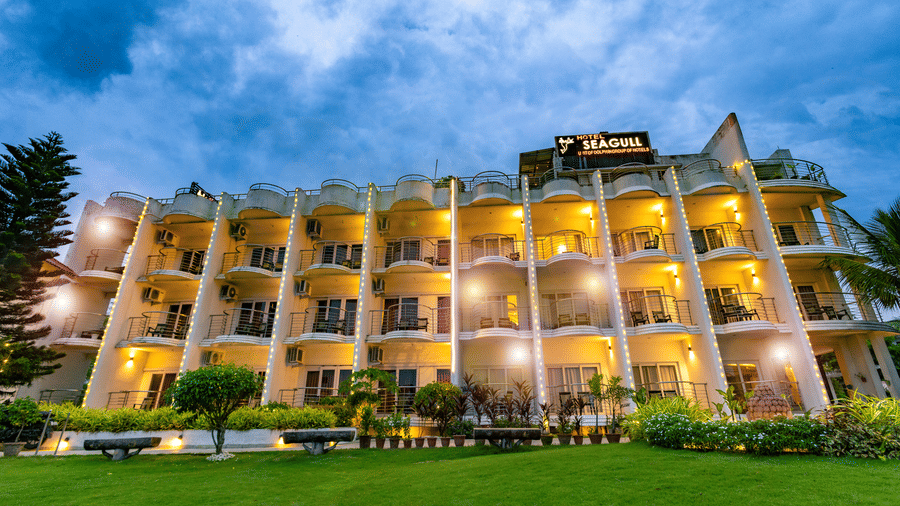 An exterior view of the multi-storey building with balconies and a lawn in front at Hotel Seagull Digha.
