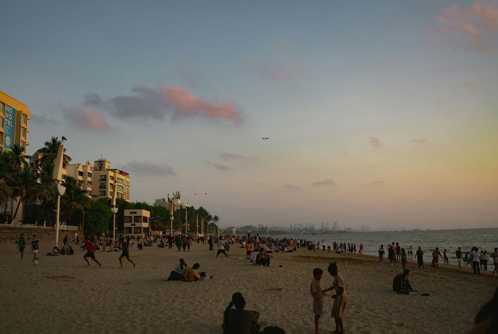 An overview of Juhu Beach with many people on it and skyscrapers in the distance.