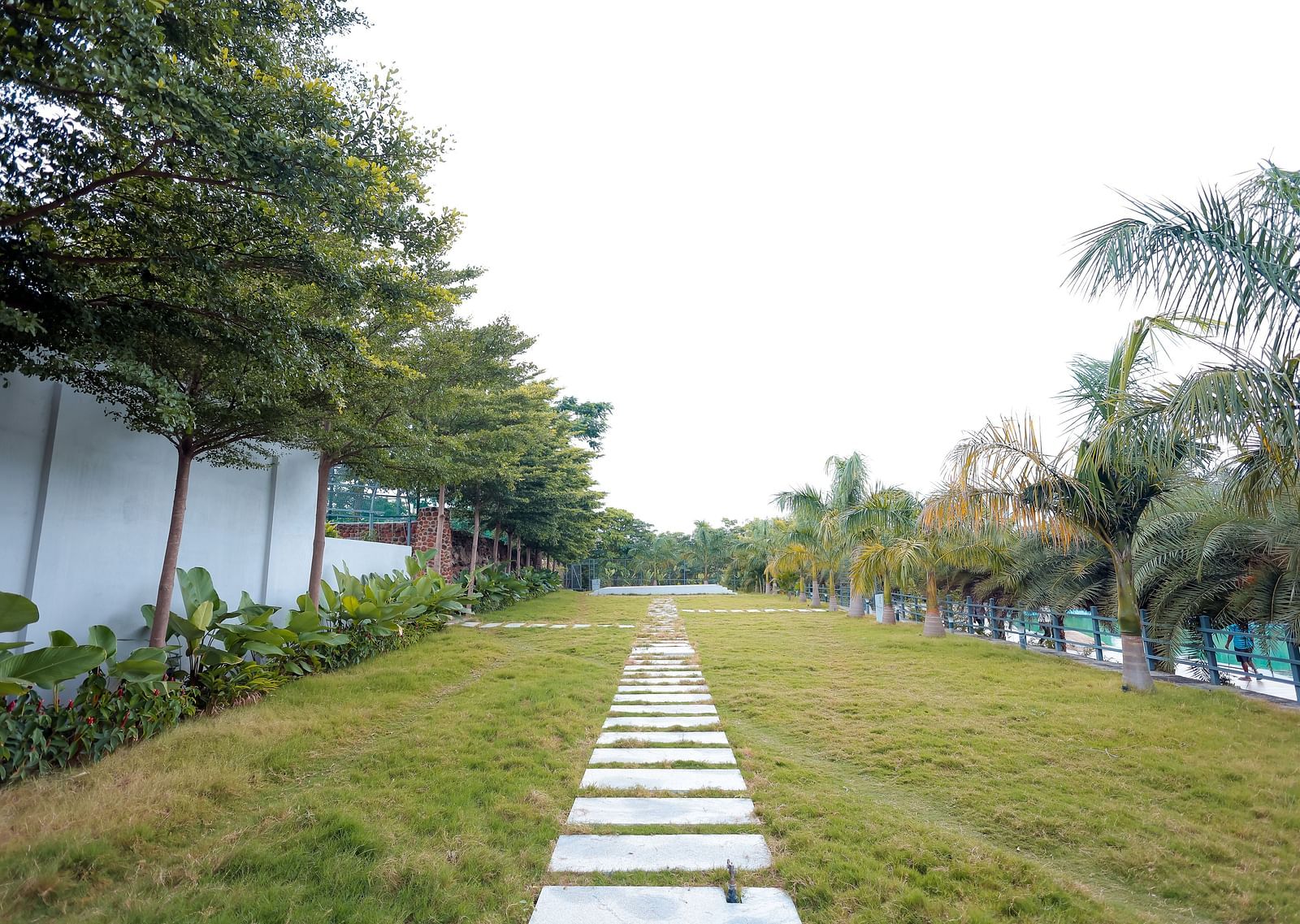 Garden pathway lined with trees and grass at Trishvam Symphony, Krishnagiri.