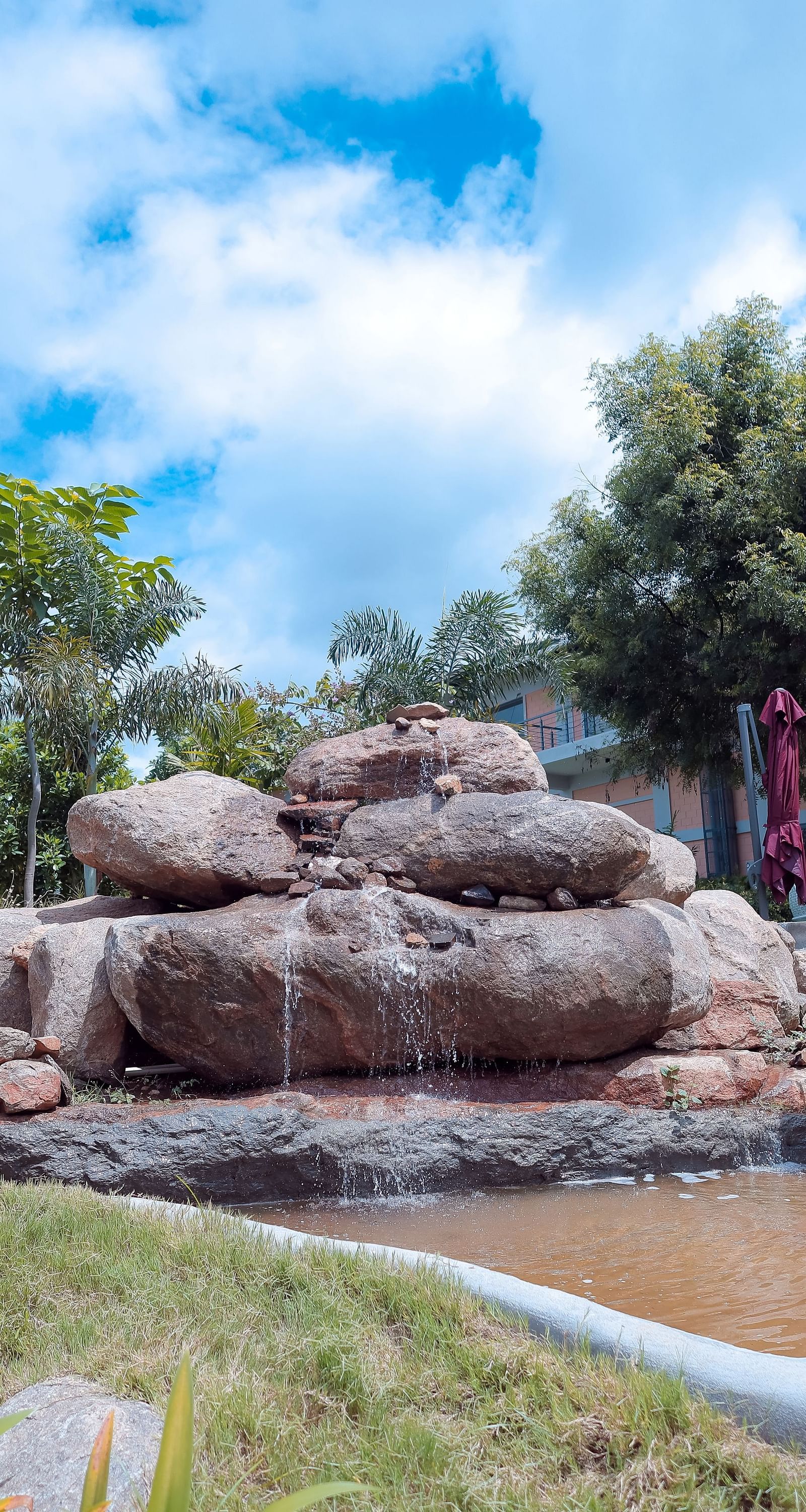 Rock waterfall feature surrounded by landscaped greenery at Trishvam Symphony, Krishnagiri.