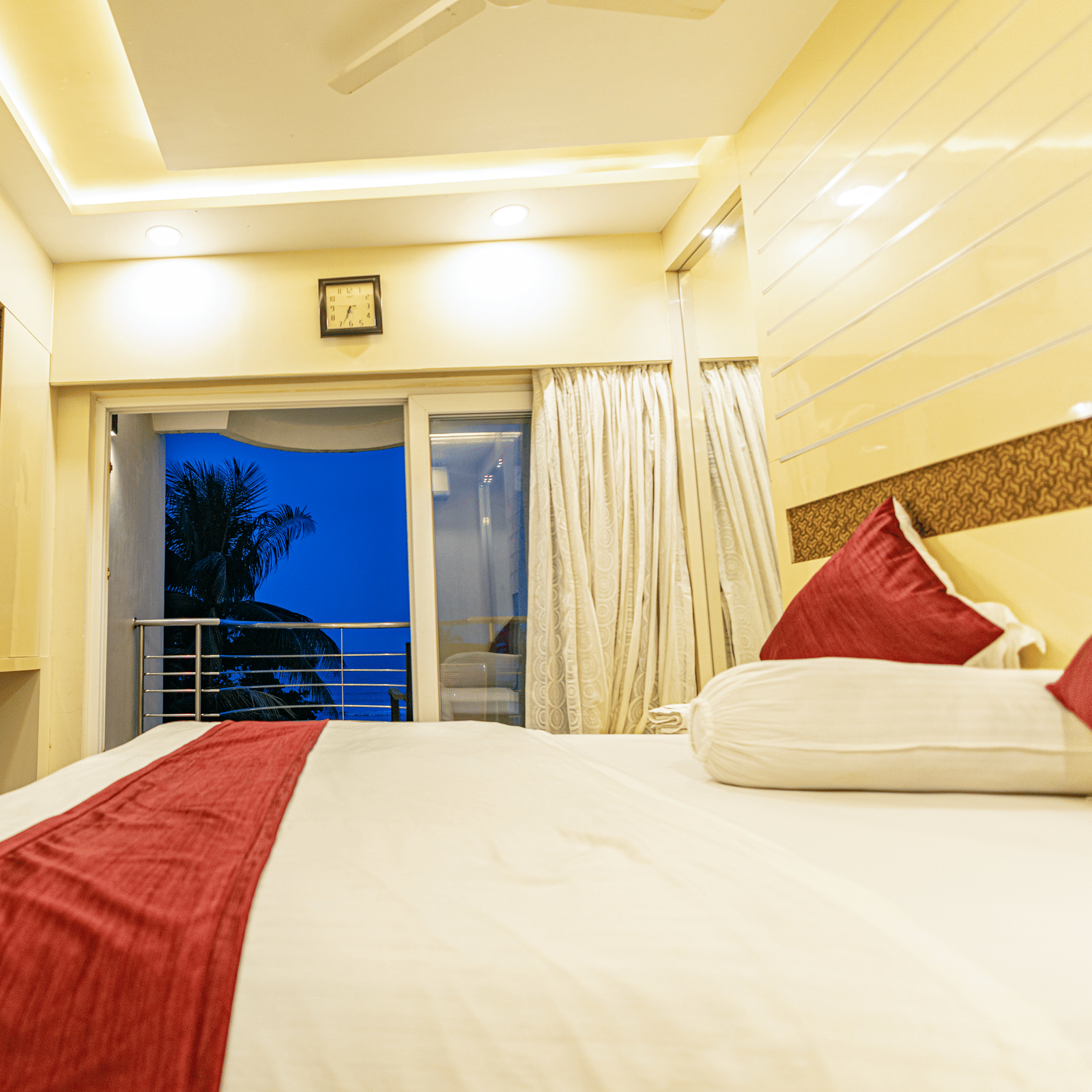 A bedroom with a king size bed with bedding, a television, and a window leading to a balcony at Hotel Seagull Digha.