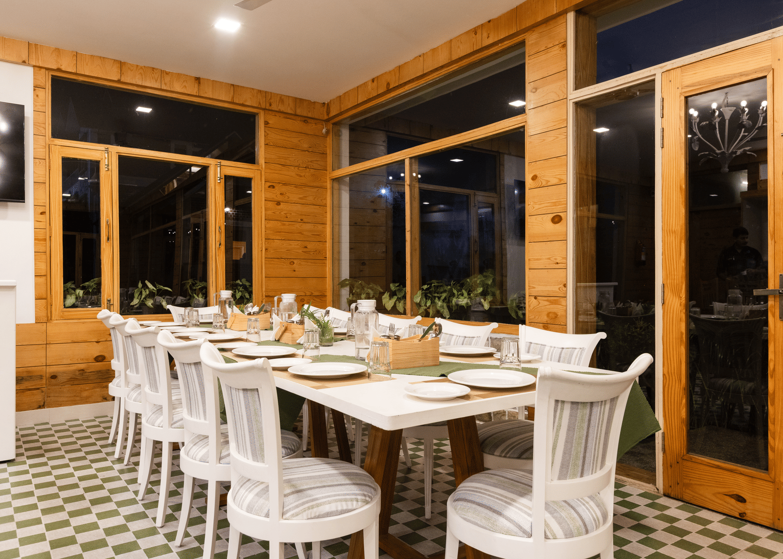 A brightly lit dining room with wooden panelling, doors, and a long table set with white chairs - Megha Resort & Villas, Dehradun