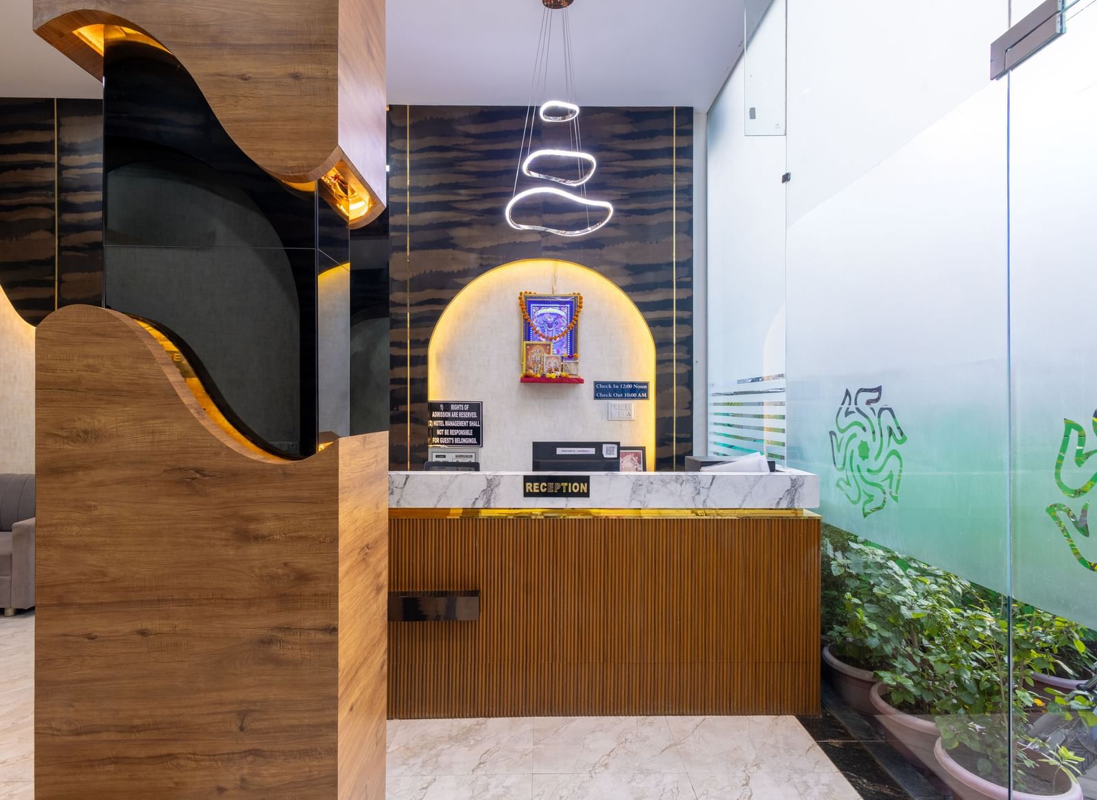 Reception desk with wall art, hanging lights and glass entrance at Pravasa Stay Dewas Naka, Indore.