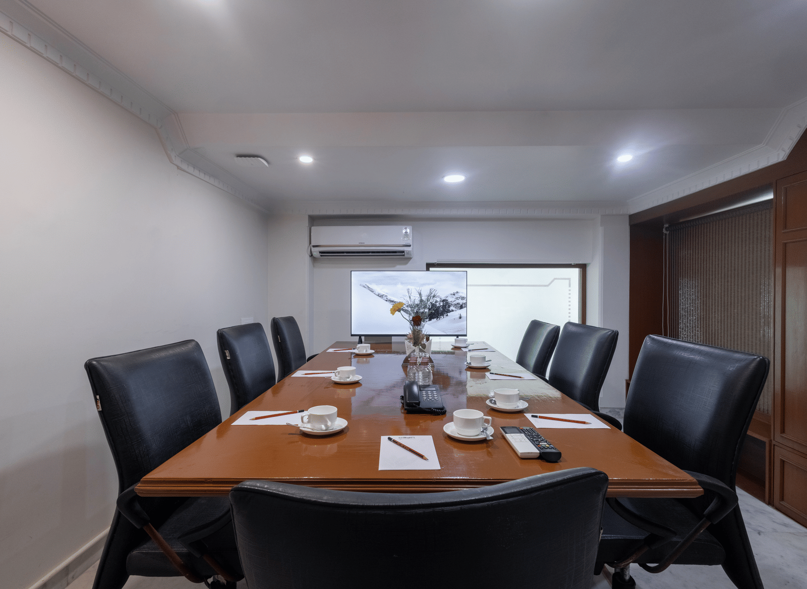 A private meeting room with a large wooden table, set for a meeting with black leather high-backed chairs at Pravasa Stay, Vadodara.