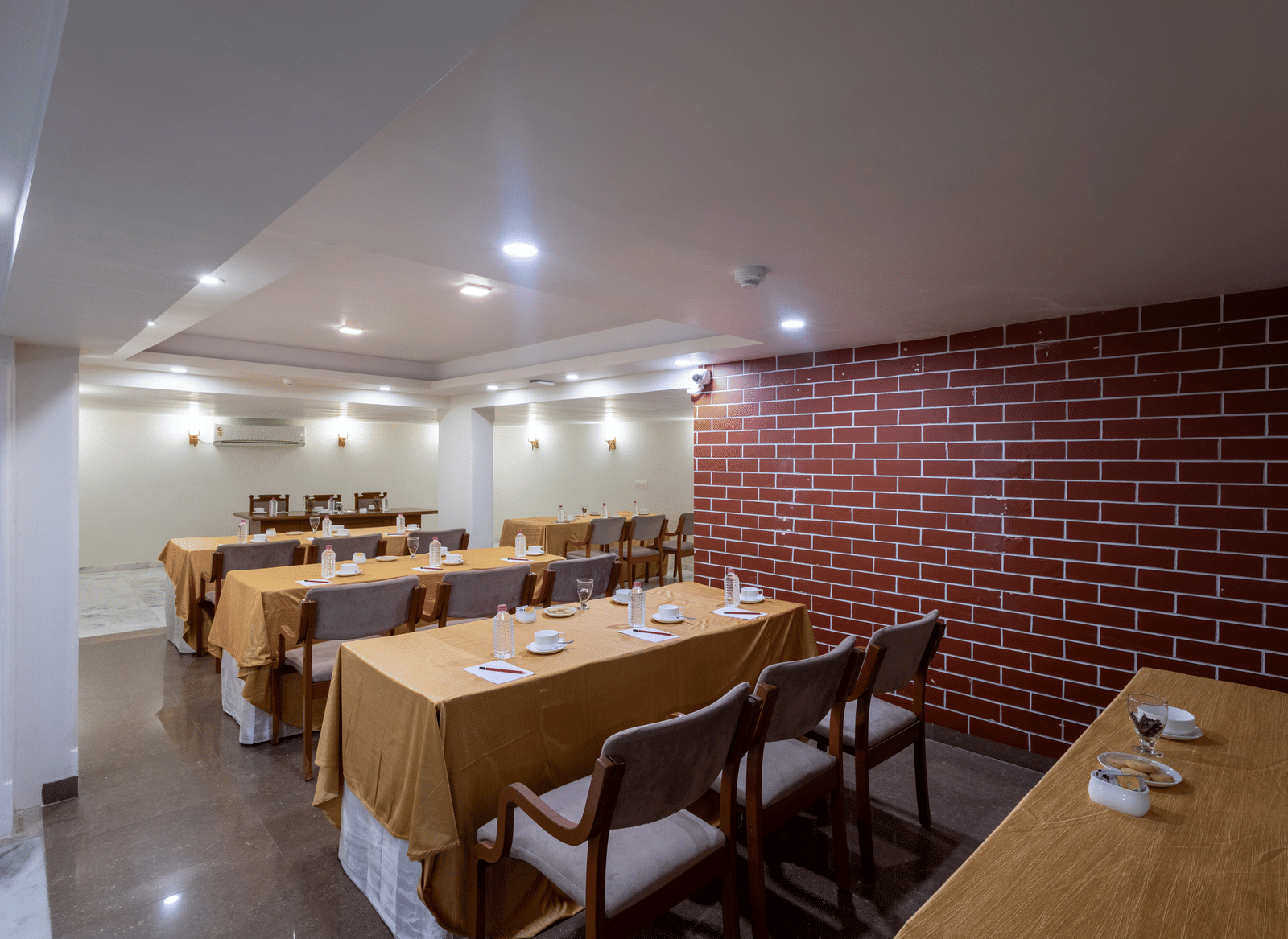 Dining space configured with long tables and chairs, covered in orange cloth, suitable for a meeting or group event at Pravasa Stay, Vadodara.