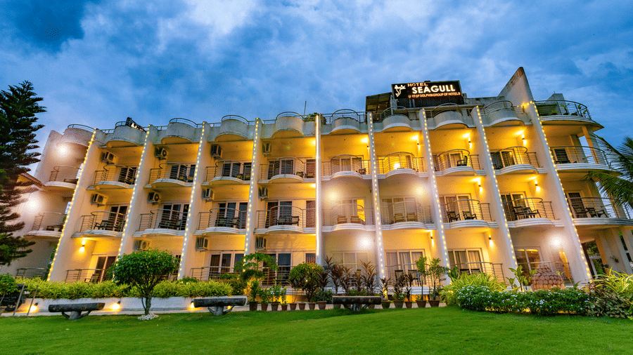 An exterior view of the multi-storey building with balconies and a lawn in front at Hotel Seagull Digha.