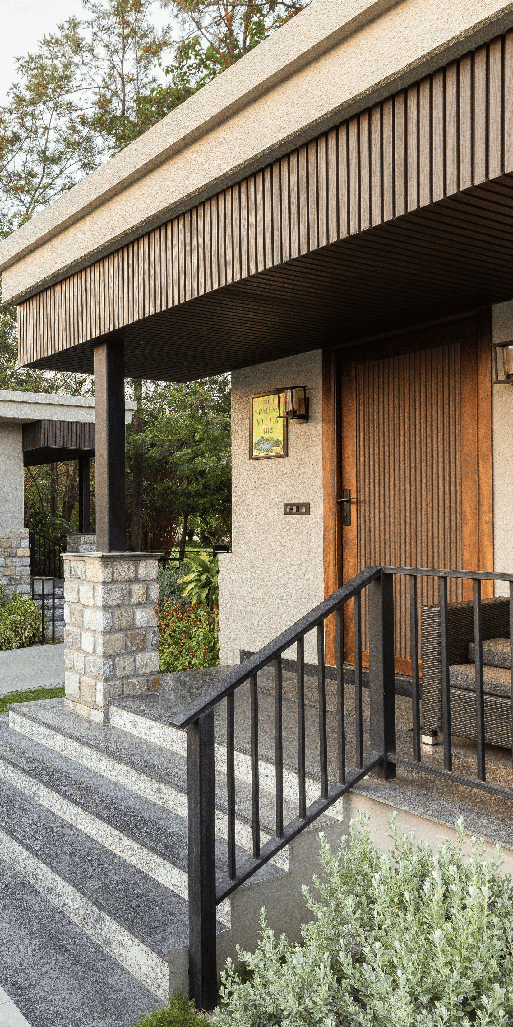 Exterior of jungle spring villa with curved stone pathway leading up to the entrance of a building with stairs and metal railing  at The Golden Tusk, Jim Corbett