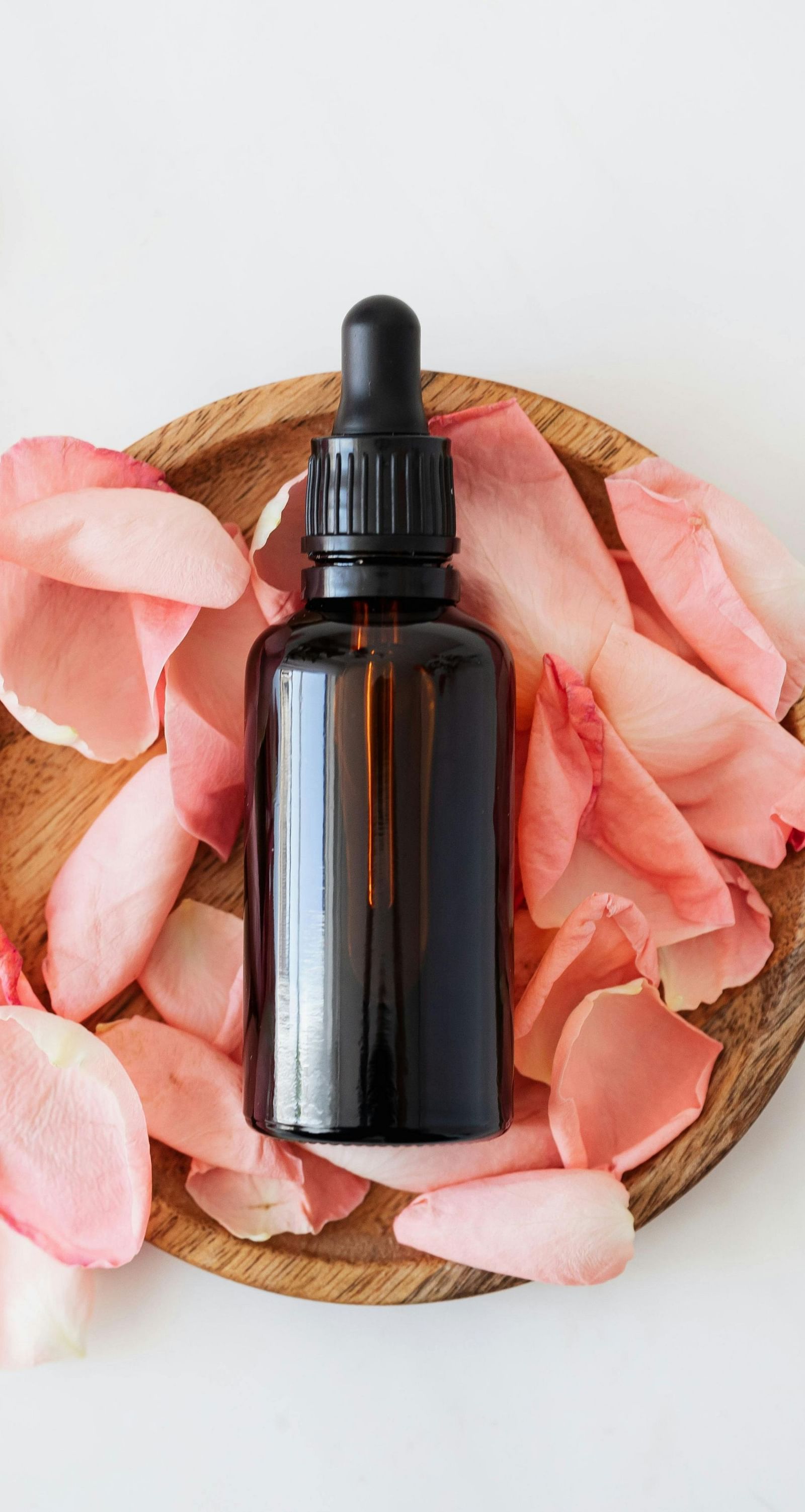An image of an essential oil in a wooden bowl with rose petals which is used for massage