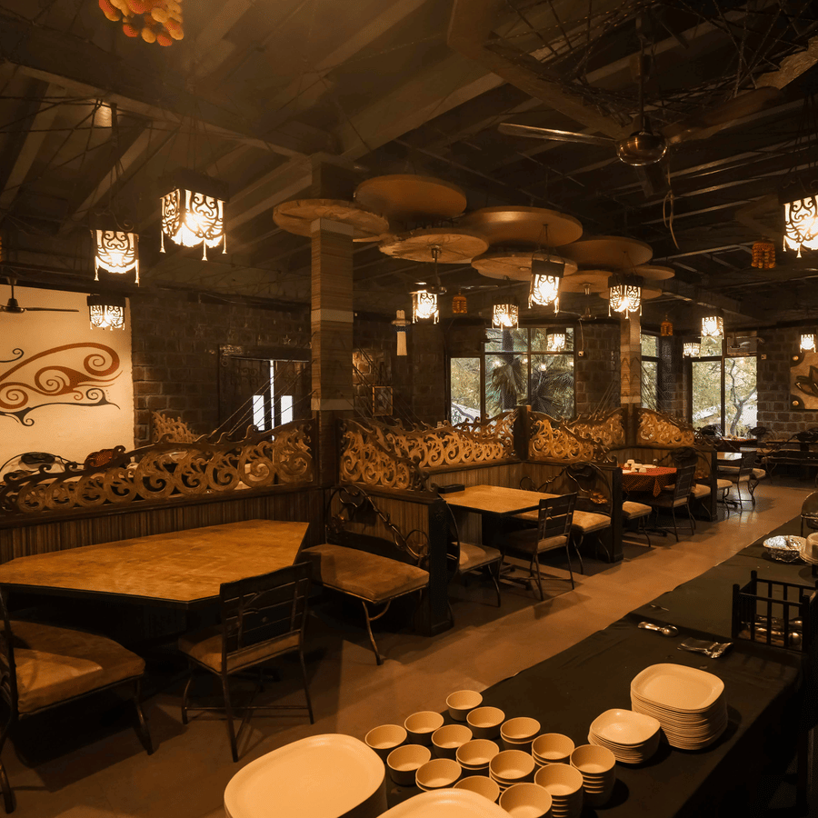 A wide view of dining area of Adamo The Village featuring rustic decor, ceiling lights, and wooden furniture arranged neatly in rows.
