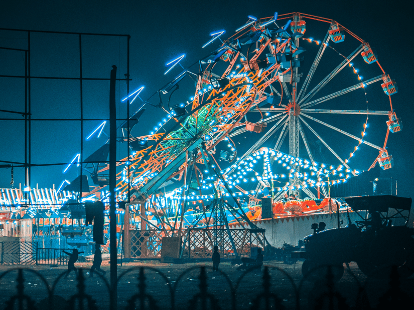 A large, brightly lit Ferris wheel spins against a dark evening sky at a fairground.