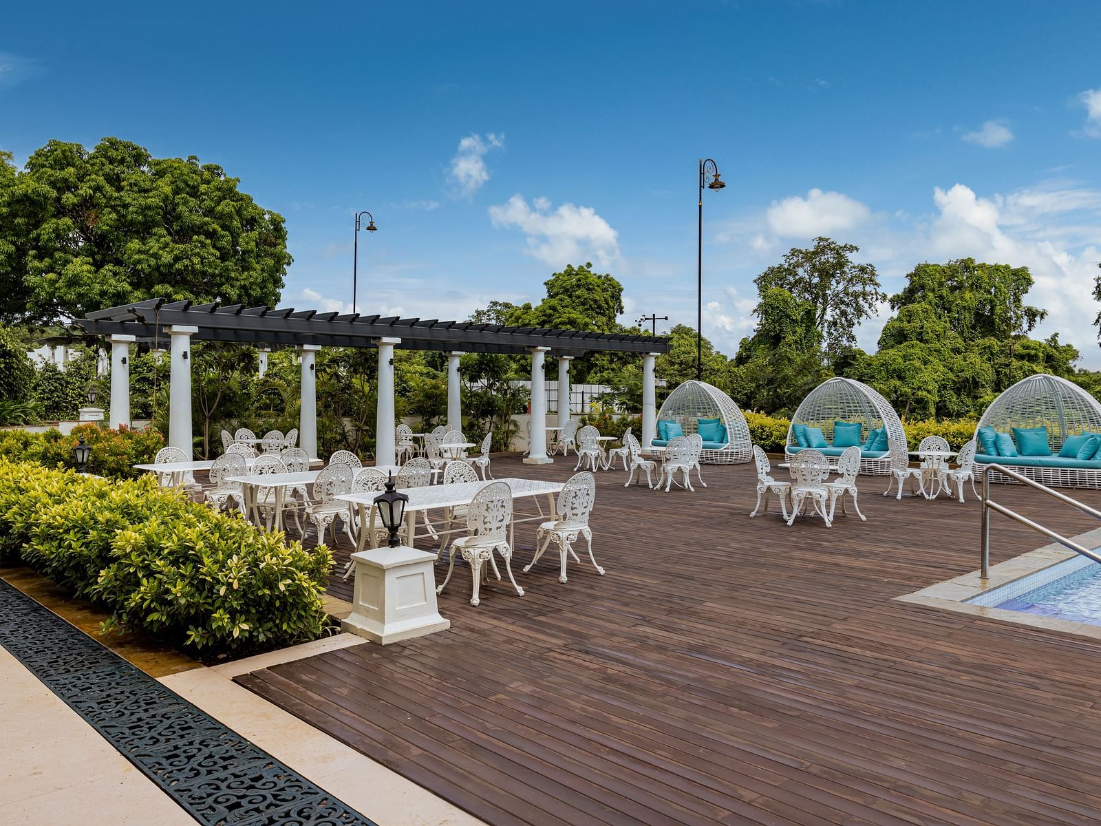 An outdoor dining area on a wooden deck right beside the pool with a bright blue sky in the background at the Imperial Goa.