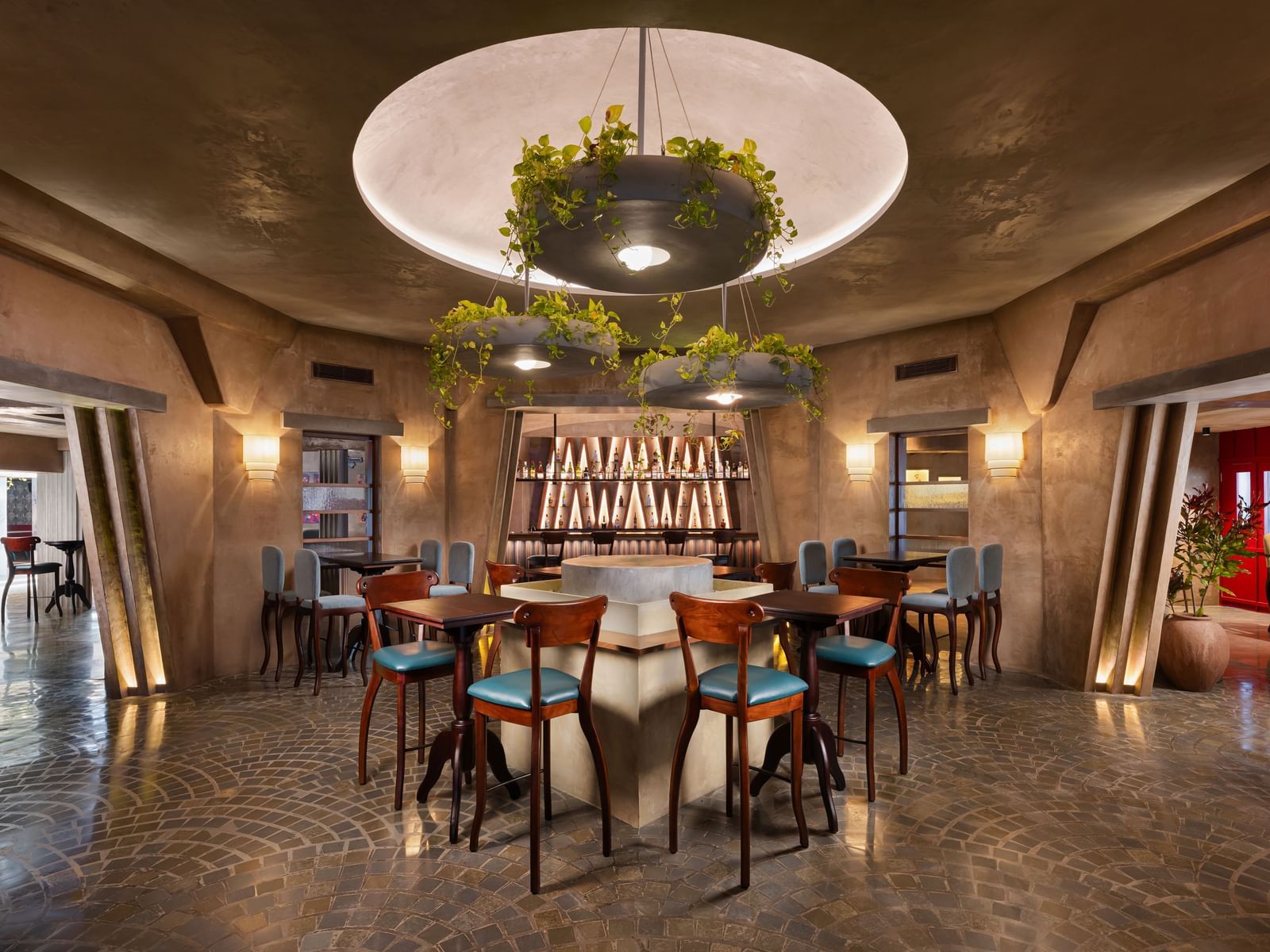 A bar area at Shilton International, Kochi, with a central round bar, stools, and hanging plant decorations.