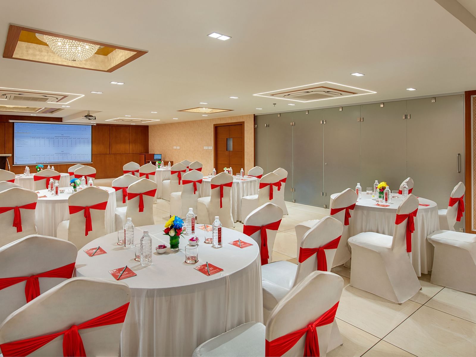 A brightly lit banquet hall set up with round tables and decorated chairs, ready for an event - SK Lords Inn Ahmedabad