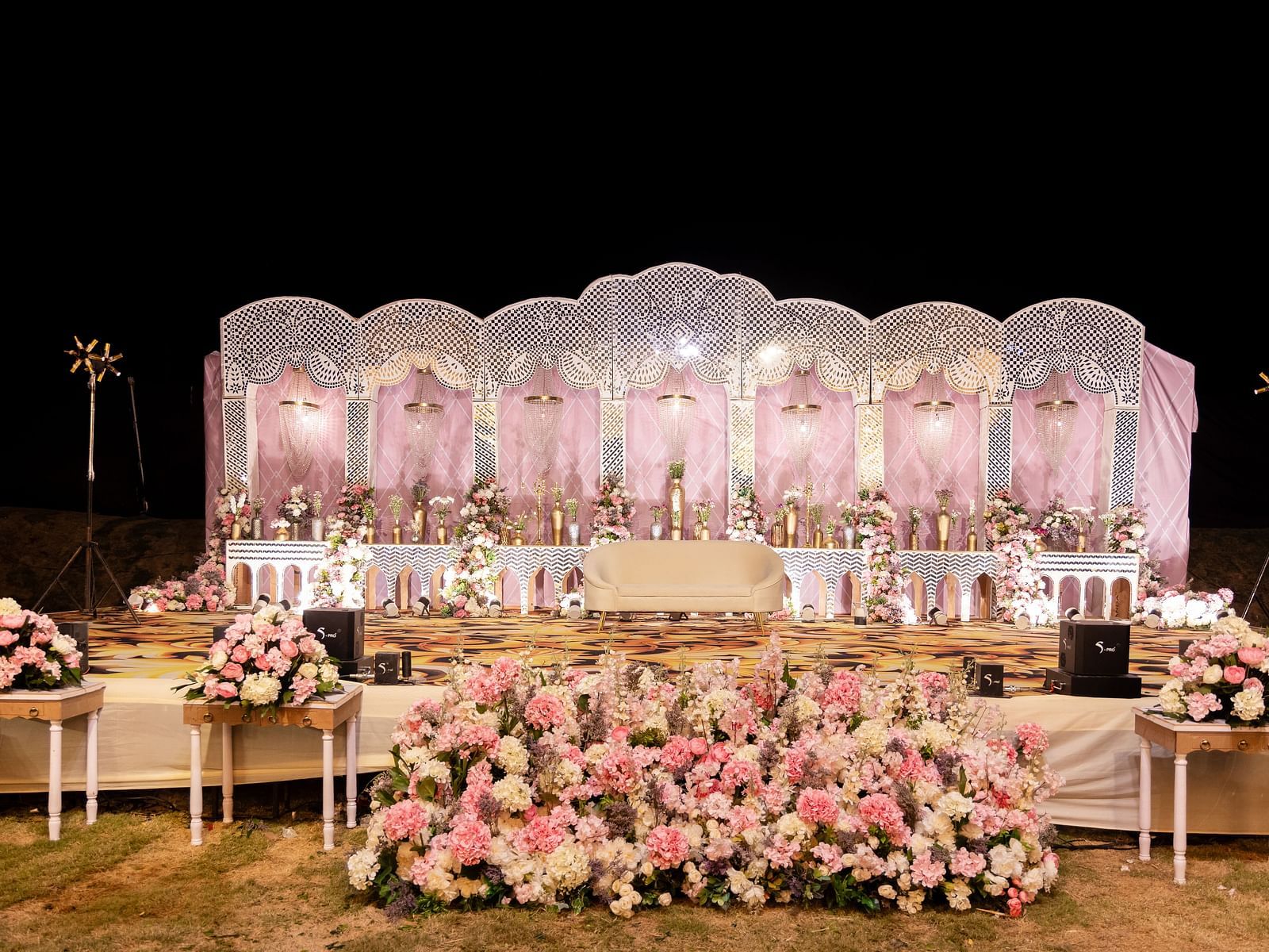 An outdoor wedding setup is shown at night, featuring a stage, seating, and floral arrangements |The Qualia Resort Club & Brewery, Udaipur