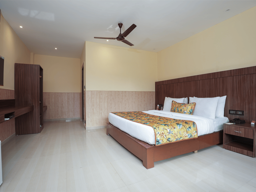 Premium Room with a large bed, wooden furniture and storage, mini fridge, and wall-mounted TV at Summit Green Lake Tea Resort & Spa, Kaziranga