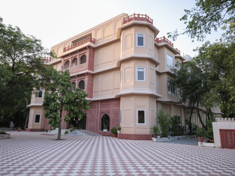 A view of the facade of Ranbanka Ballroom with a large courtyard, trees, and blue sky in the background.
