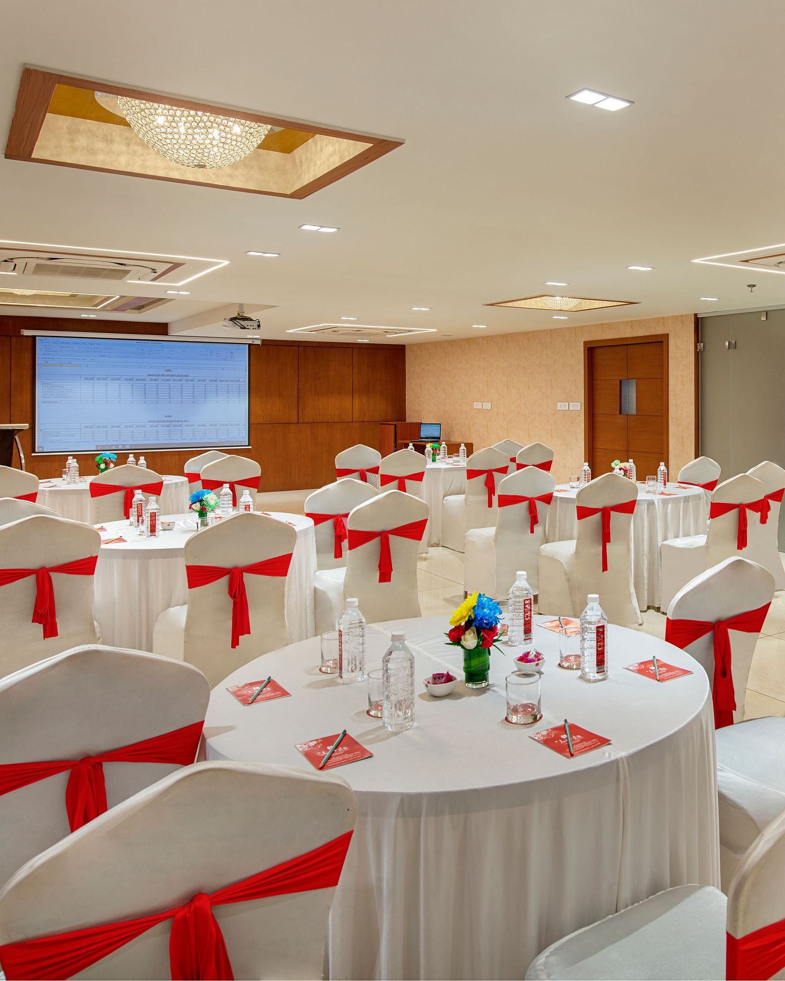 A brightly lit banquet hall set up with round tables and decorated chairs - SK Lords Inn Ahmedabad