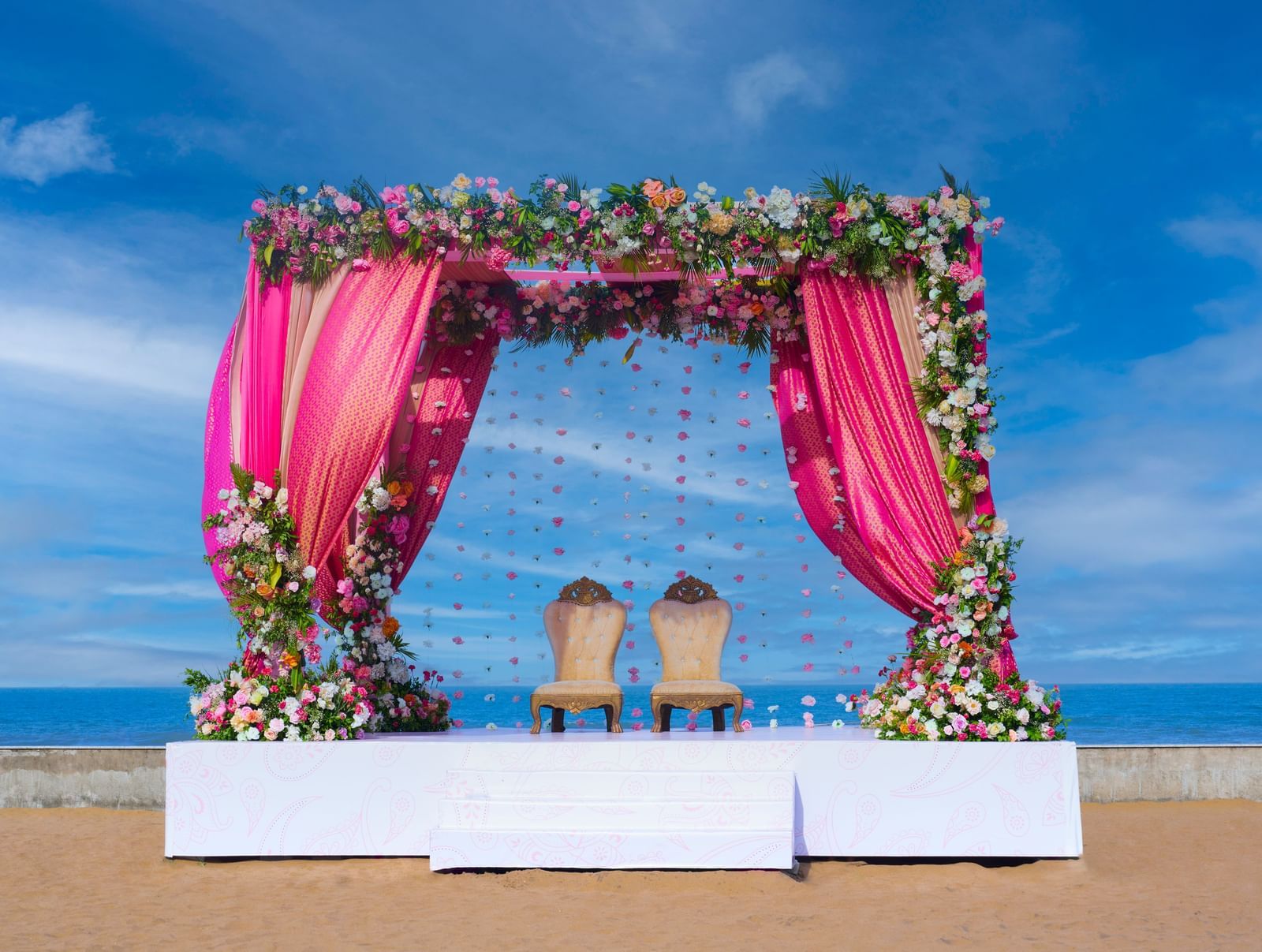 An outdoor platform stage with two chairs under the decorated patio with flowers  featuring the blue sky & sea at the backdrop at Grande Bay Resort & Spa.