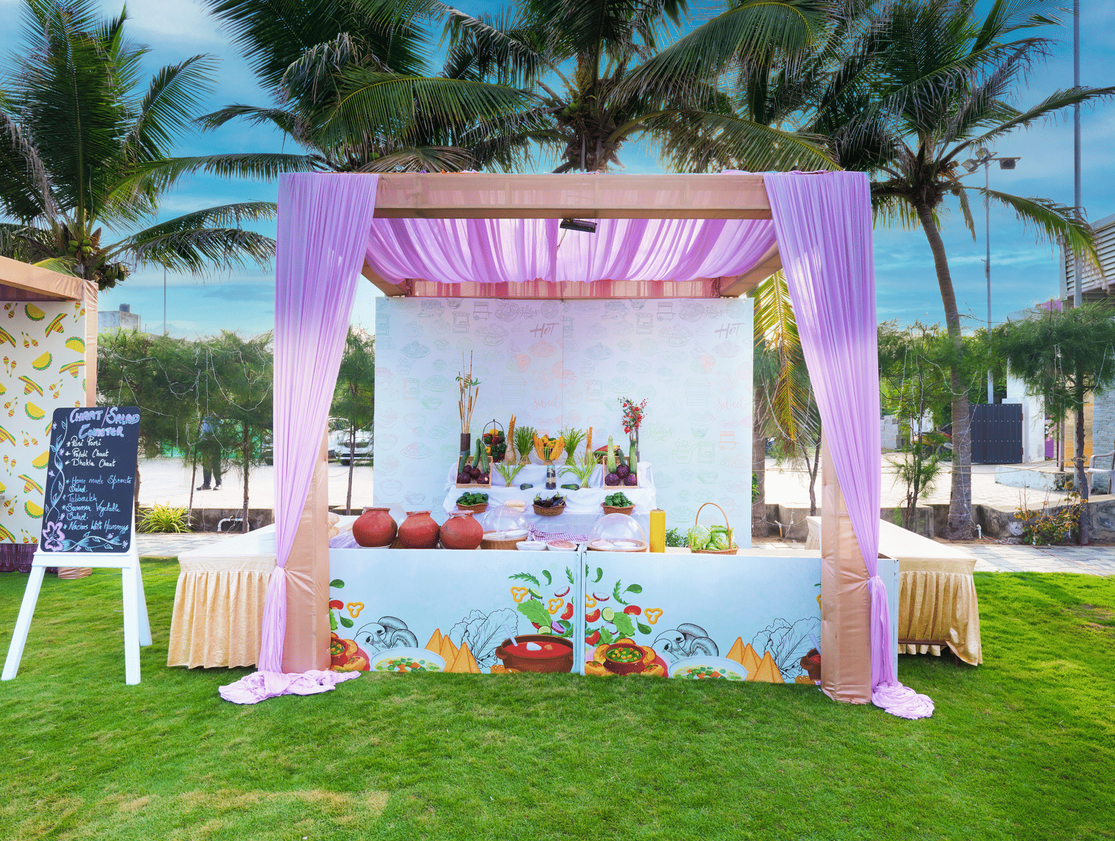 A colourful outdoor canopy decorated with drapes and flowers featuring a buffet setup on the lawn - Grande Bay Resort & Spa, Mamallapuram