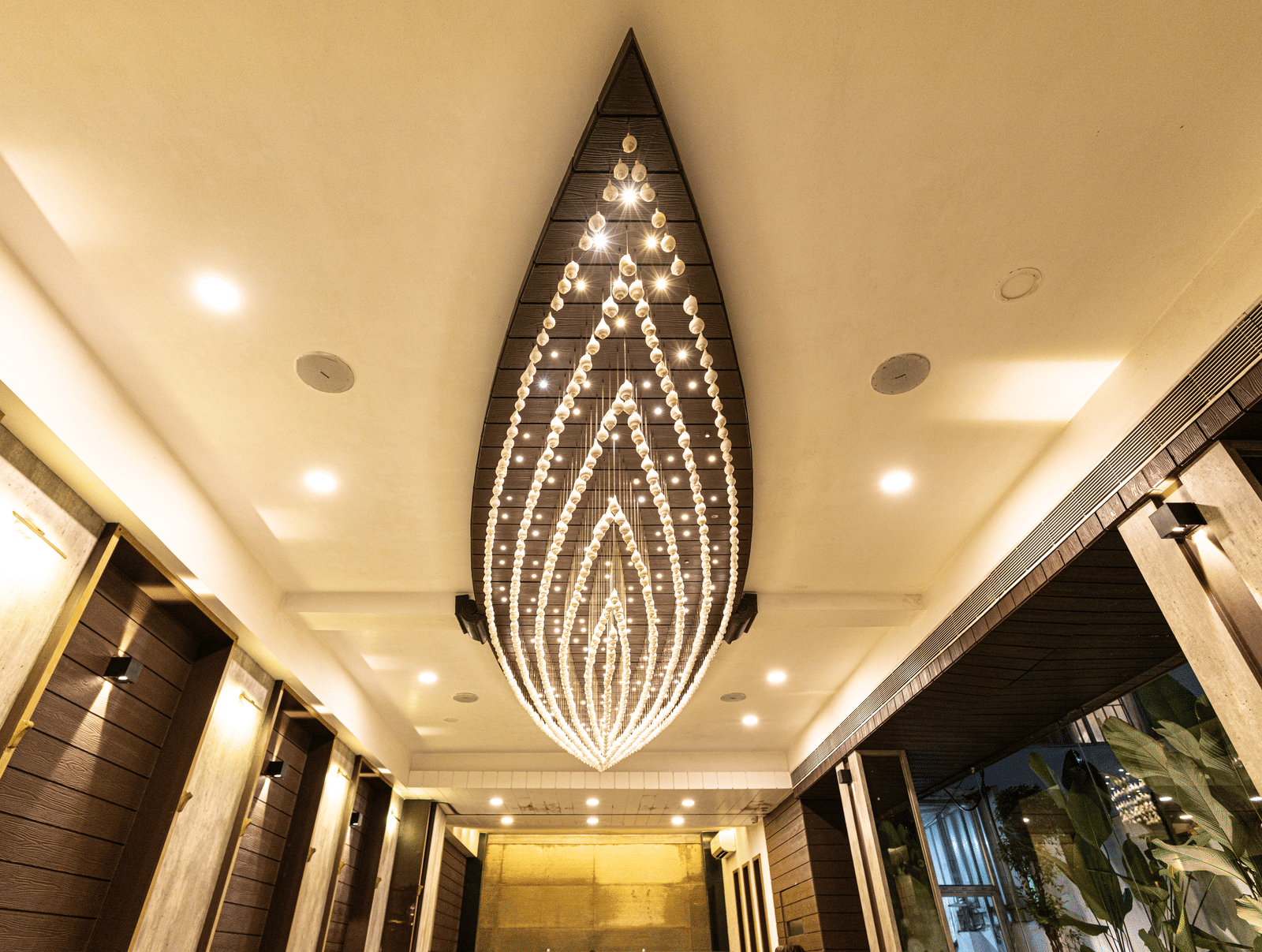 The ceiling view of the dining area at Hotel Seagull Digha showing a long decorative chandelier, lighting, and corridor walls on both sides.