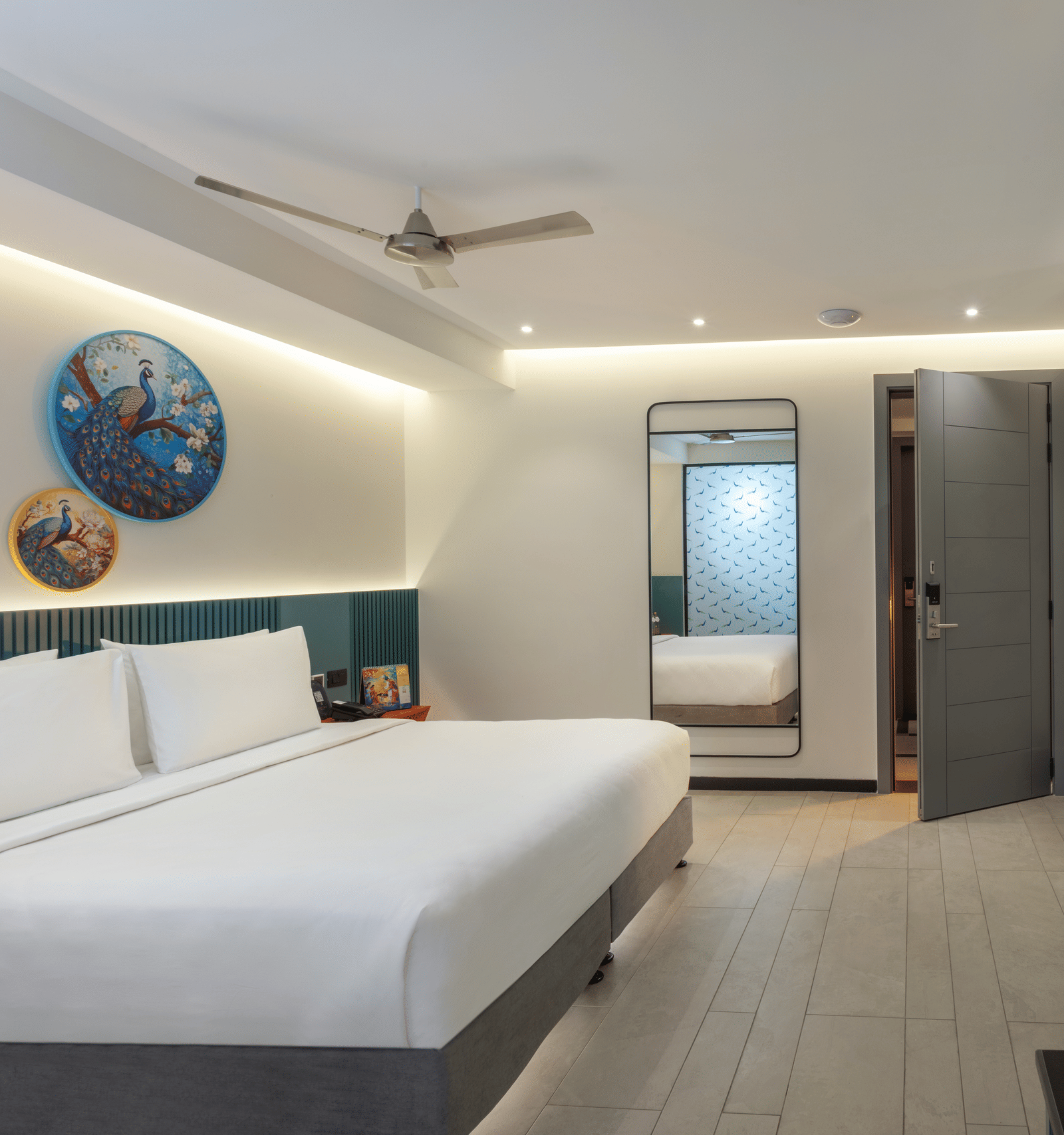 A hotel room featuring a well-made bed, a mirror on the wall, a television, a work desk, and an open door | Zibe Luxe Hyderabad by GRT Hotels 
