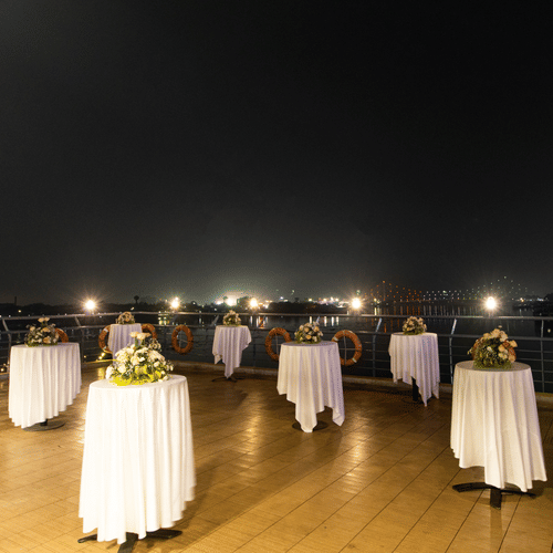 Compass Deck - Rooftop event space at night with tables set for an outdoor gathering, overlooking city lights -  Polo Floatel Kolkata