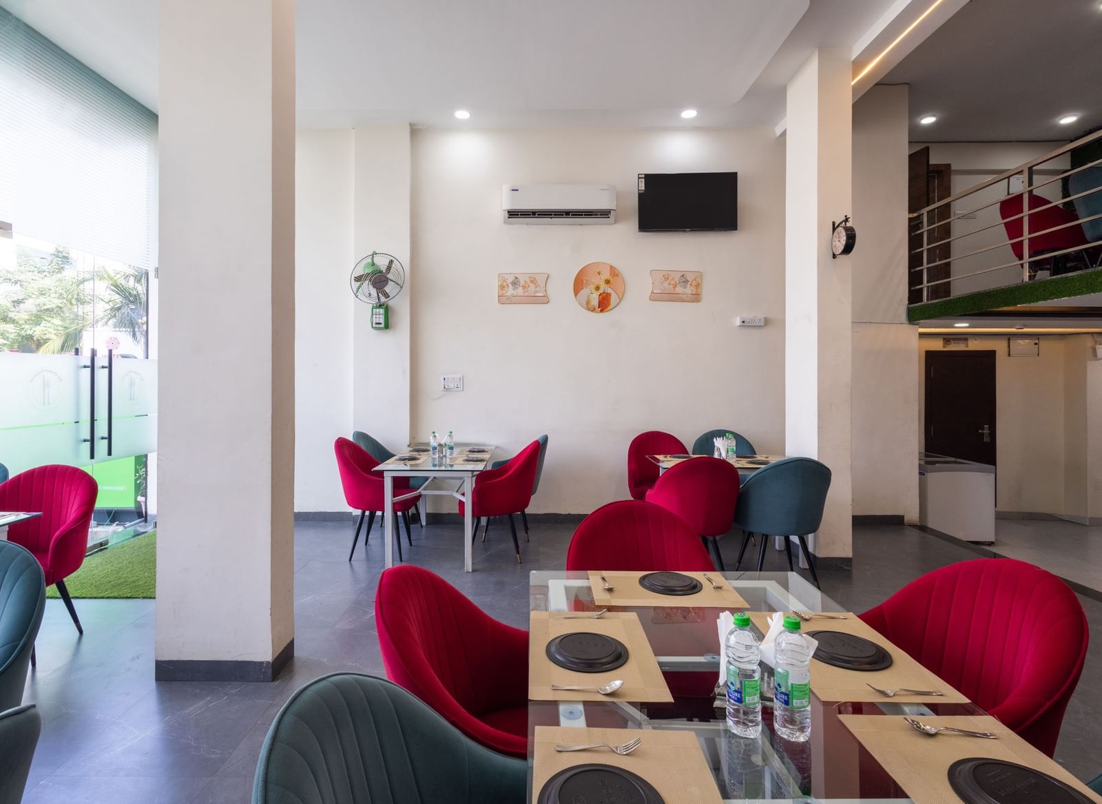 Indoor dining space with red and blue chairs around tables near glass doors at Pravasa Stay Dewas Naka, Indore.
