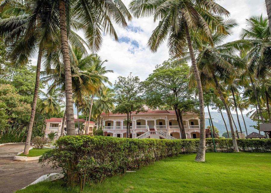 Expansive green lawn with coconut trees, leading to a shaded seating area with a view of resort buildings in the background - Black Thunder, Coimbatore