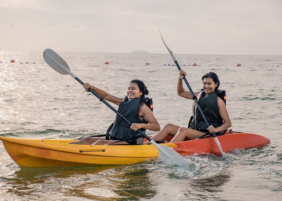 alt-text  Two women in separate kayaks on the sea, paddling with smiles, enjoying a beautiful sunset, reflecting a calm and joyful water activity.