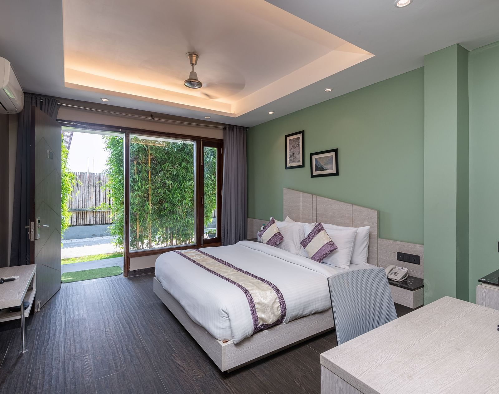 Spacious room at DLS Forest Vines Resort featuring a large bed, a bedside table, a table with chairs, and a large glass door leading to the balcony.