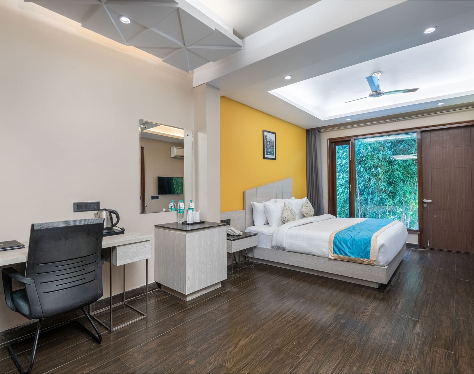 A spacious accommodation in Jim Corbett at DLS Forest Vines Resort featuring a large bed, glass windows, a desk, and a chair.