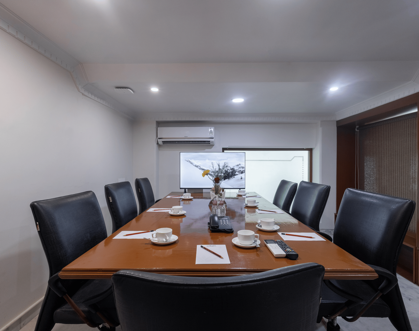 A private meeting room with a large wooden table, set for a meeting with black leather high-backed chairs at Pravasa Stay, Vadodara.