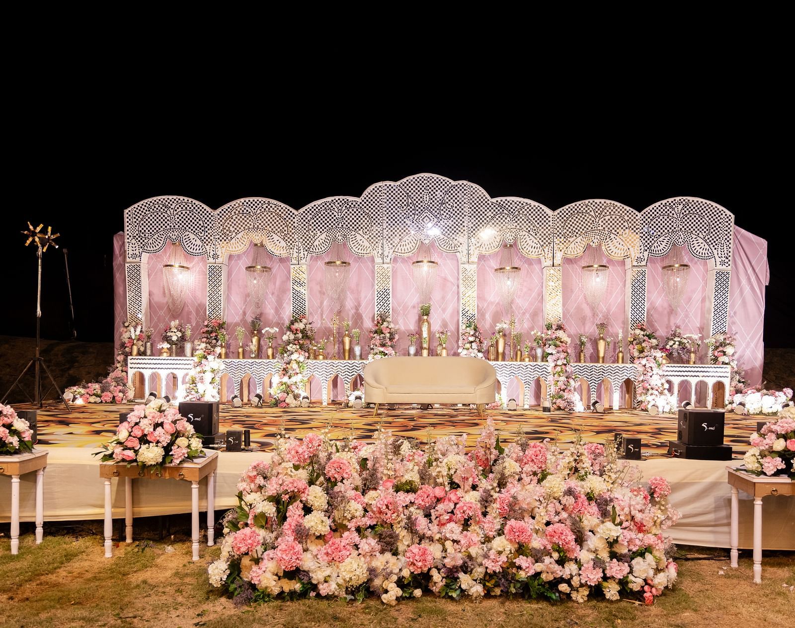 An outdoor wedding setup is shown at night, featuring a stage, seating, and floral arrangements |The Qualia Resort Club & Brewery, Udaipur