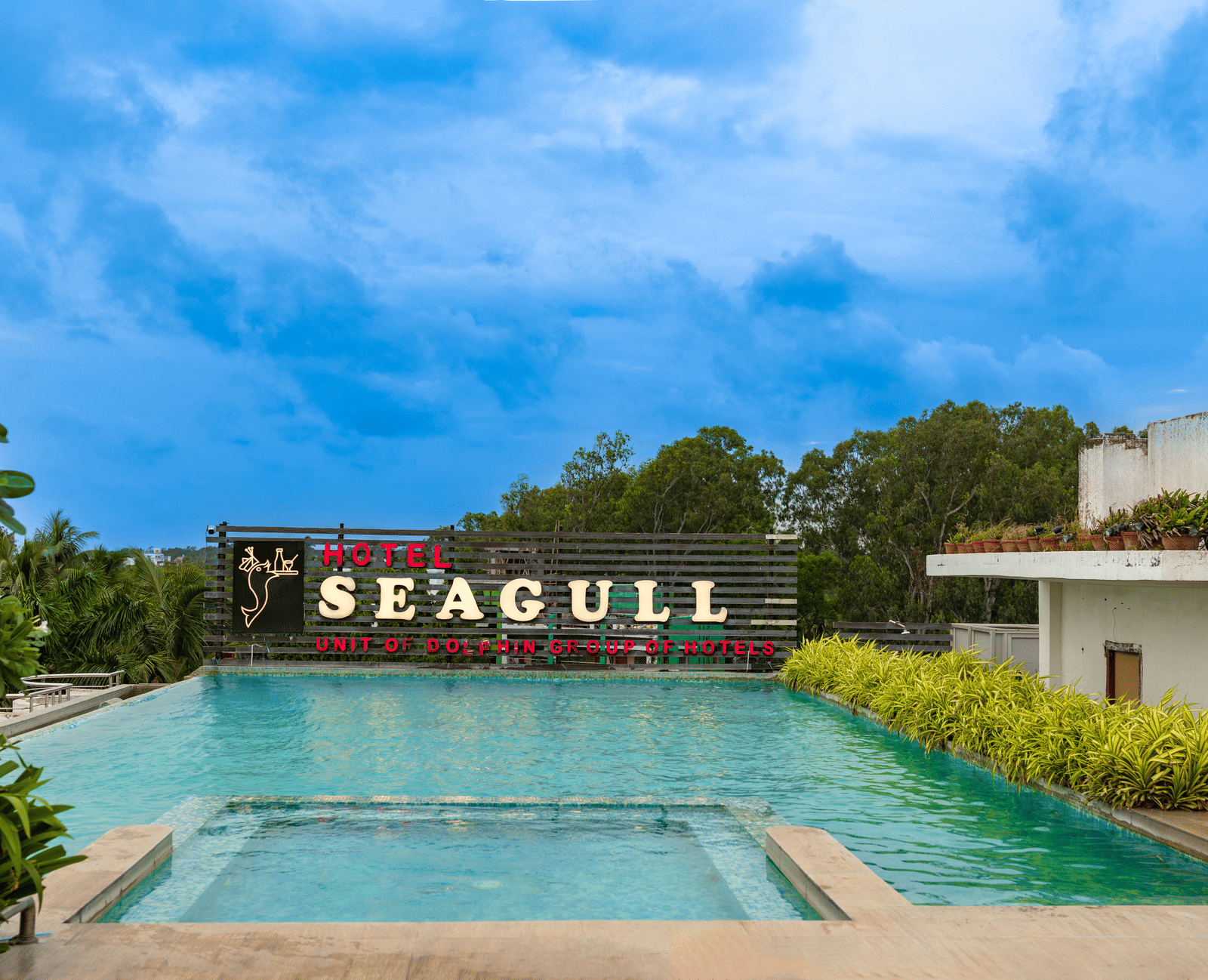 A swimming pool in front of the building with the ‘Seagull’ signage and trees in the background at Hotel Seagull, Digha.