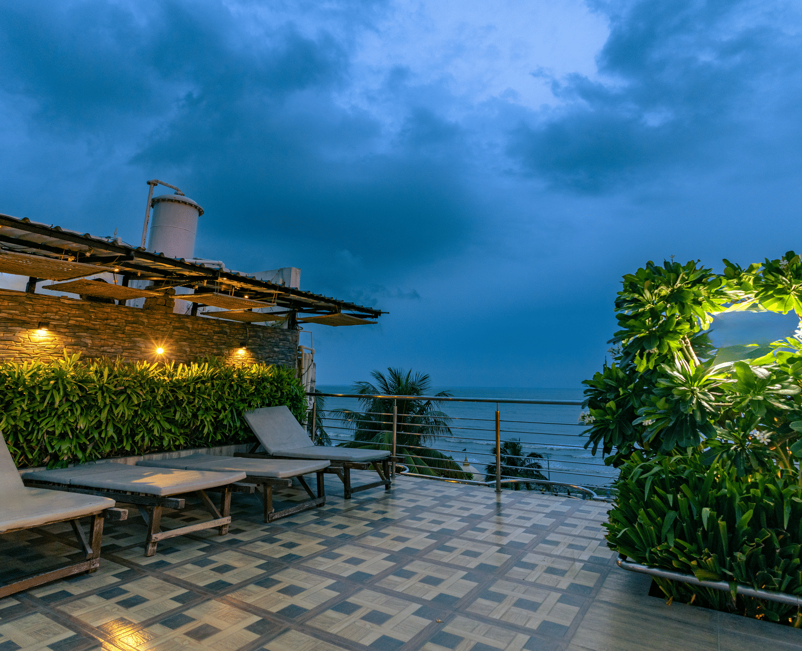An outdoor seating area with tables, sun loungers, plants and a cloudy sky at Hotel Seagull Digha.