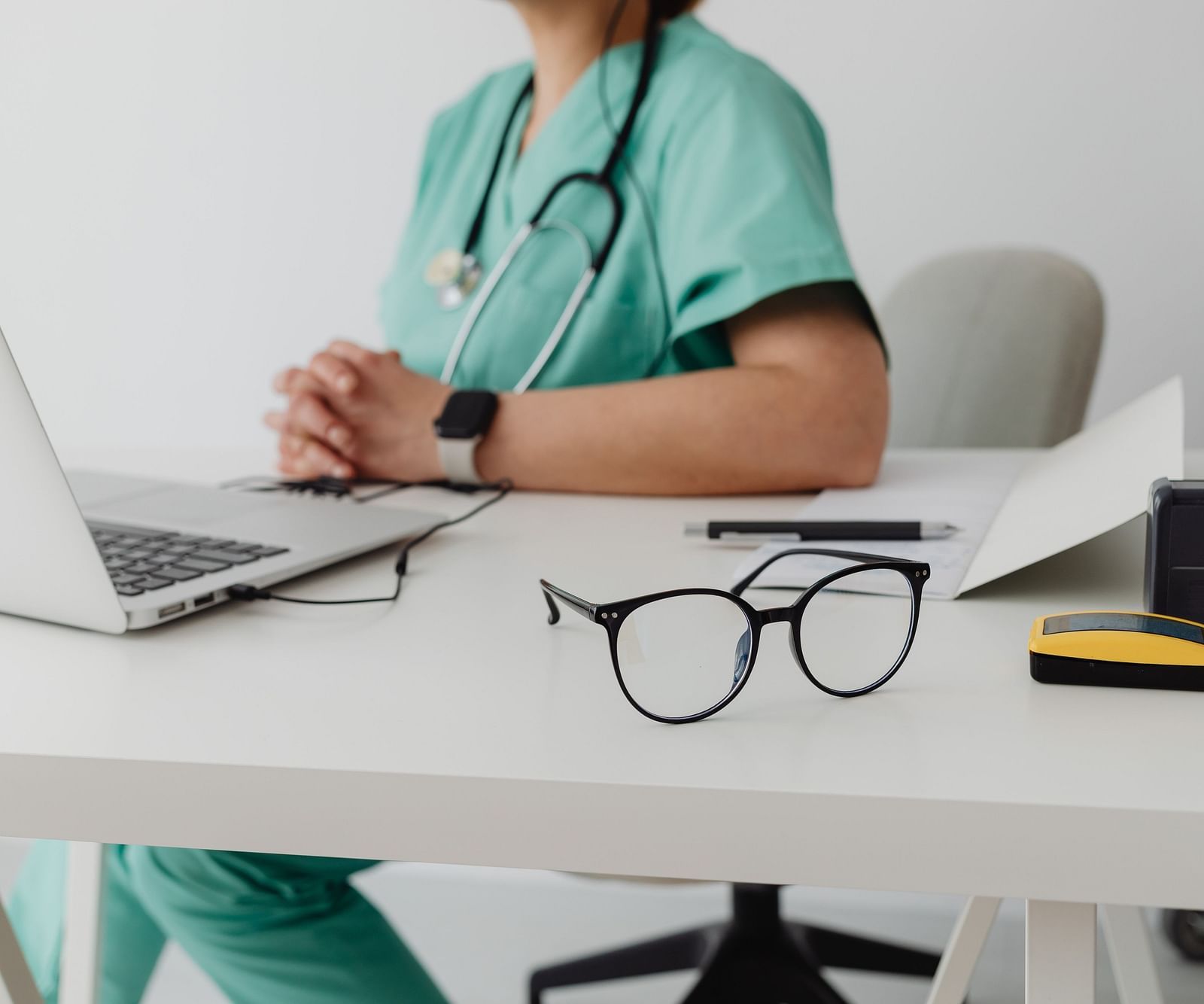A view of the doctor sitting on chair with laptop open on table.